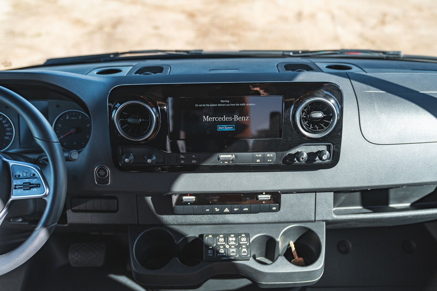 Inside an RV rental: Mercedes-Benz Sprinter dashboard with infotainment screen, climate, & custom accessory controls.