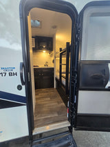 Inside a Braxton Creek 17 BH rv rental: compact kitchen with sink, microwave, and cozy bunk beds visible through the open door.