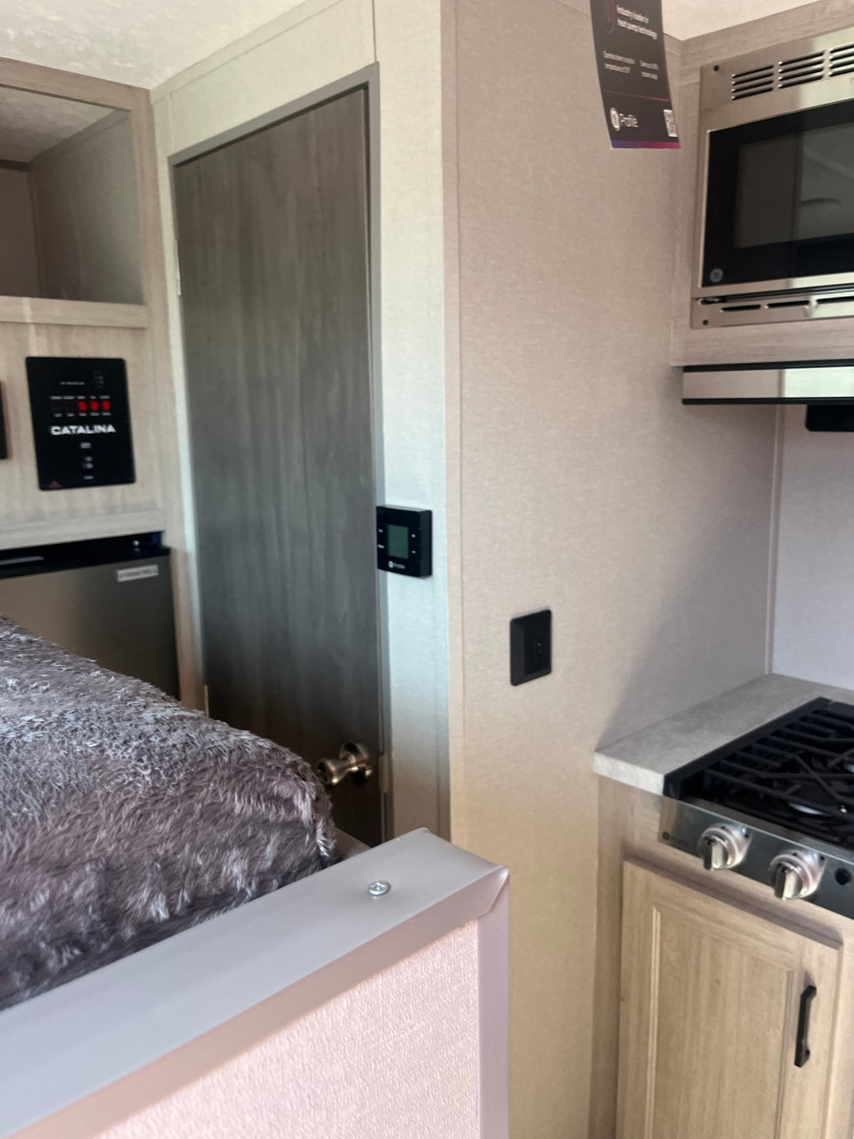 This RV rental interior features a bed, control panel (Catalina), microwave, and stovetop, showcasing practical living space. — photo 7