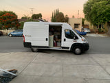 Customized Ram ProMaster campervan, potentially an rv rental, with its side door open, revealing a cozy interior parked on a residential street.