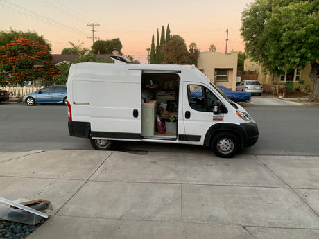 Customized Ram ProMaster campervan, potentially an rv rental, with its side door open, revealing a cozy interior parked on a residential street.