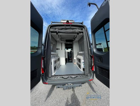 Open rear doors of a gray rv rental camper van reveal a spacious interior with modular seating and a clean gray floor, ready for travel.