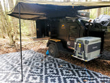 An RV rental overland trailer campsite with outdoor kitchen, Truma fridge, awning, and ground mat. Perfect for off-grid adventure!