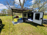 A cozy RV rental teardrop trailer with an awning setup for comfortable camping outdoors.