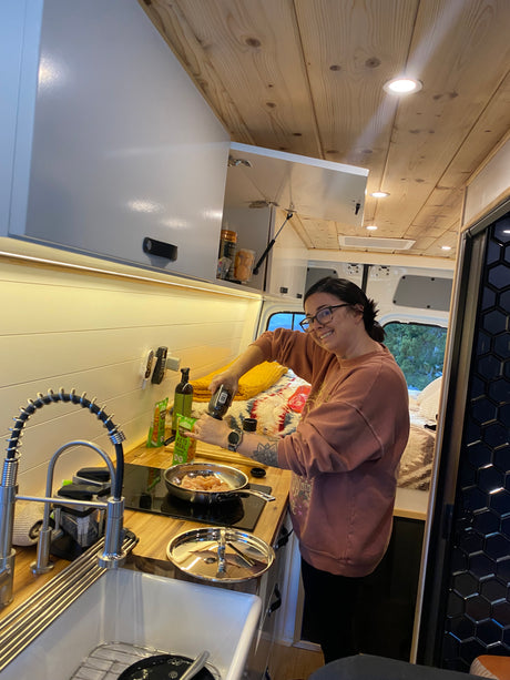 Smiling and seasoning dinner in a compact RV rental kitchen, ideal for mobile cooking during van life adventures.