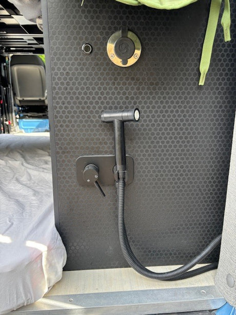This RV rental van's flexible shower setup includes a quick-connect port, handheld head, hose, and water controls on a black panel.