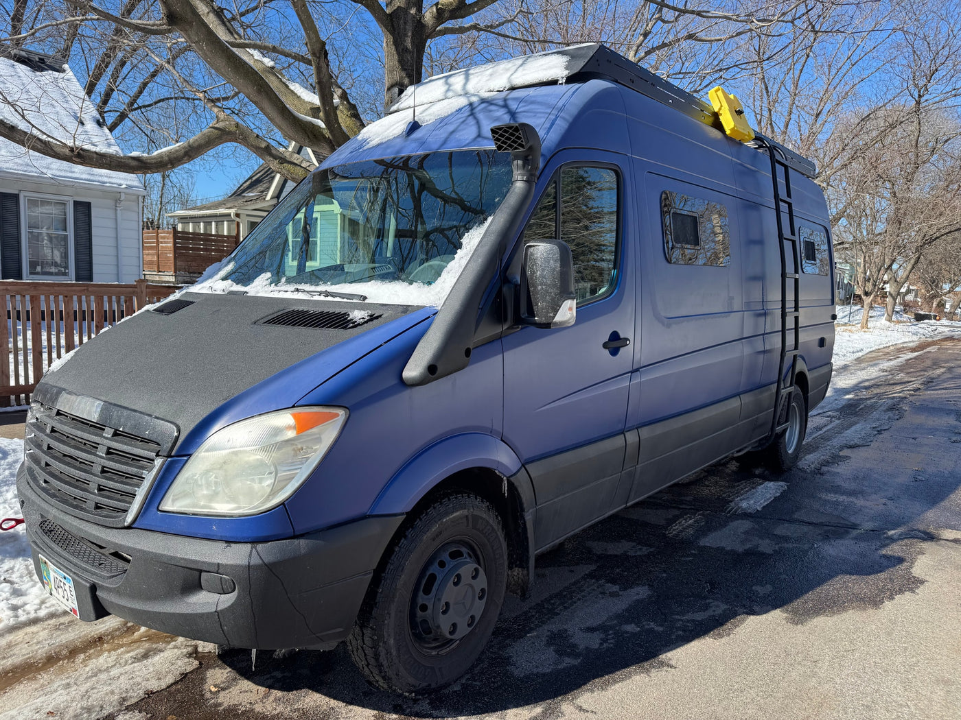 Custom blue Mercedes-Benz Sprinter camper van with snorkel, roof rack, and ladder, on a snowy street. Ideal RV rental. — photo 10