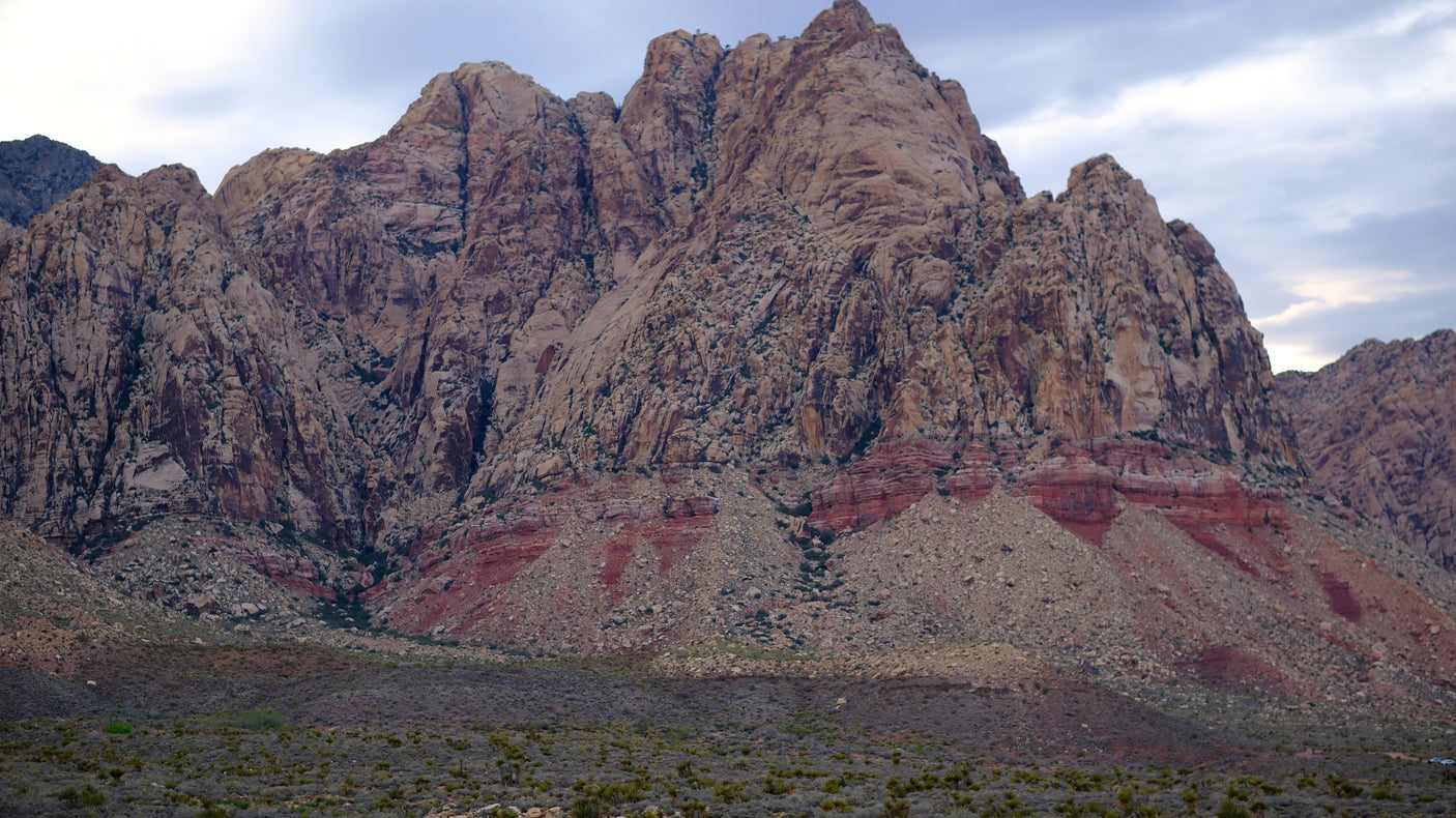 Rugged red rock mountains with layered strata rise from the desert. Explore this vast landscape with an RV rental.