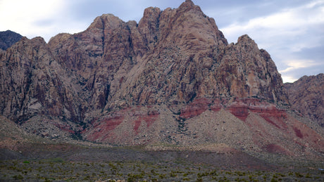 Rugged red rock mountains with layered strata rise from the desert. Explore this vast landscape with an RV rental.
