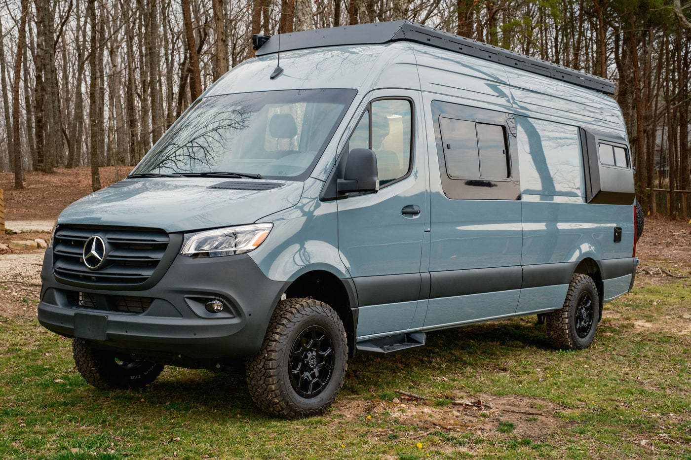 Adventure awaits! This grey Mercedes-Benz Sprinter camper van is available for rv rental, parked among trees with rugged tires. — photo 5