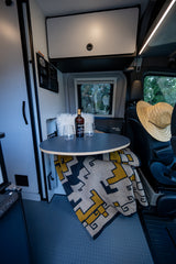 Cozy rv rental interior featuring a table, Kopke Port, glasses, & a patterned blanket. Ready for travel!