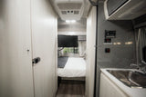 Clean rv rental interior featuring a bedroom with TV, and a kitchen area with sink and solar controls for comfortable travel.