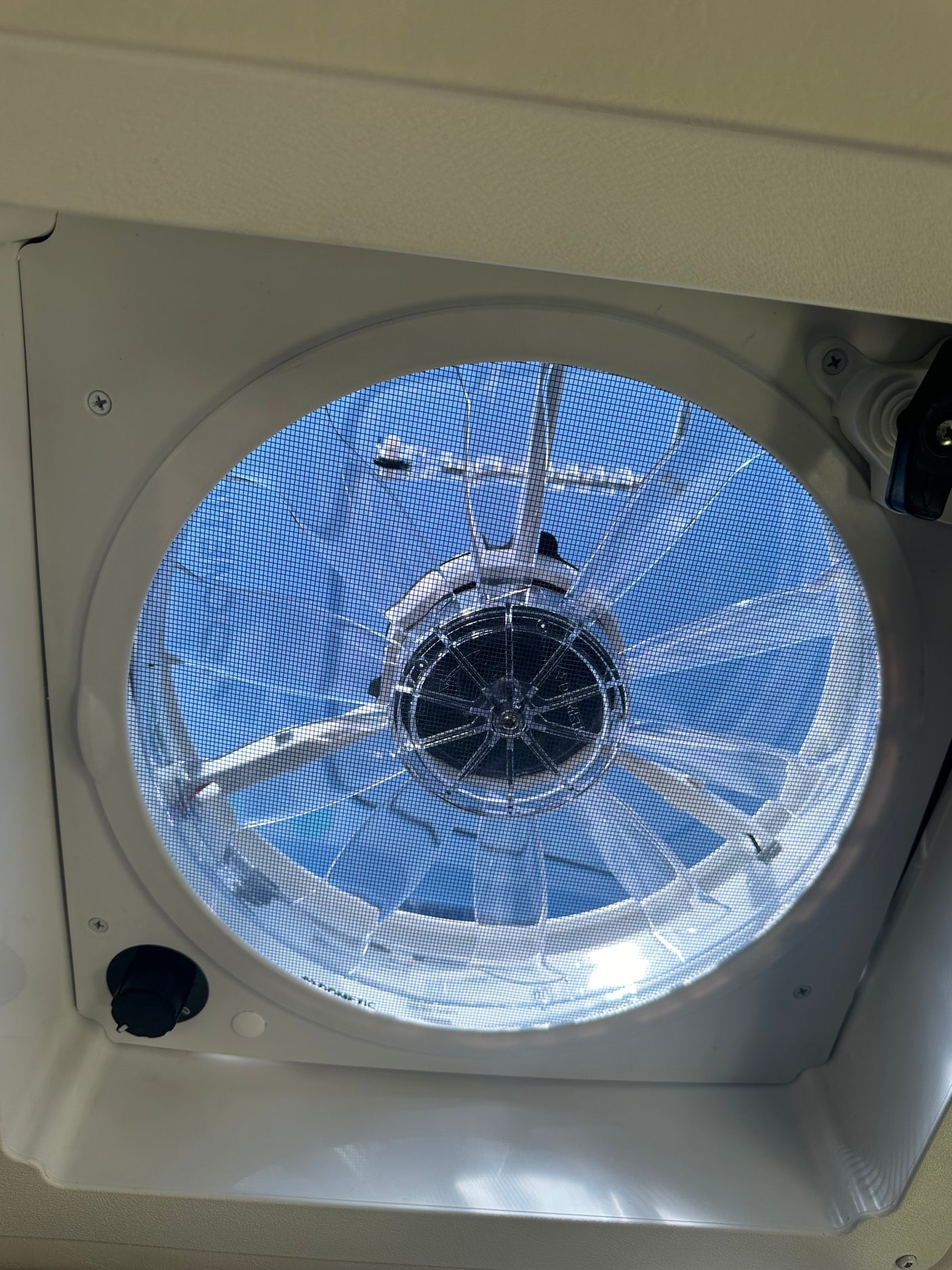 Inside an RV rental: a ceiling vent fan with screen, offering views of the clear blue sky.