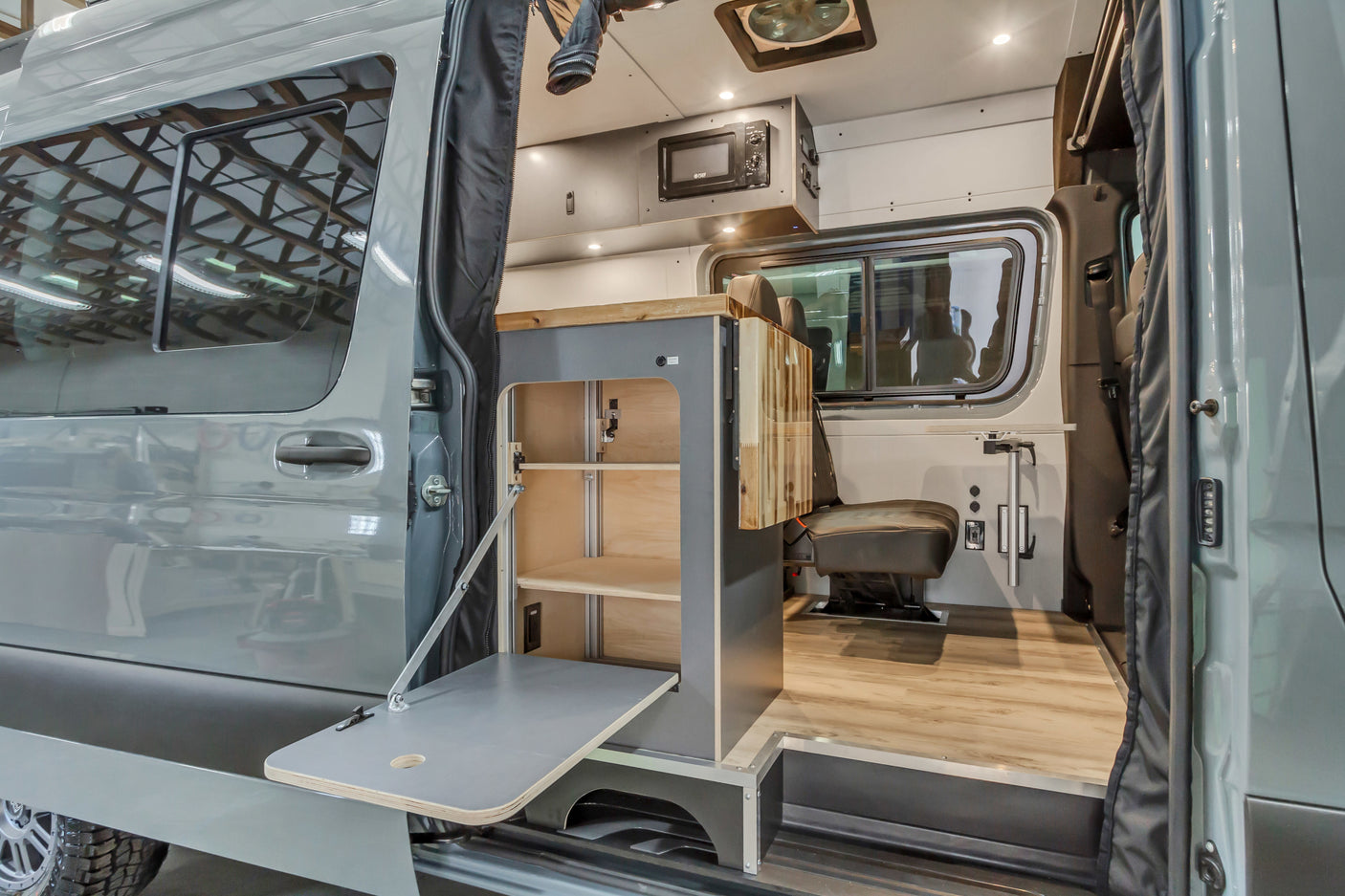 Step into this modern RV rental campervan conversion, featuring modular interior cabinets, a fold-out table, and cozy seating.