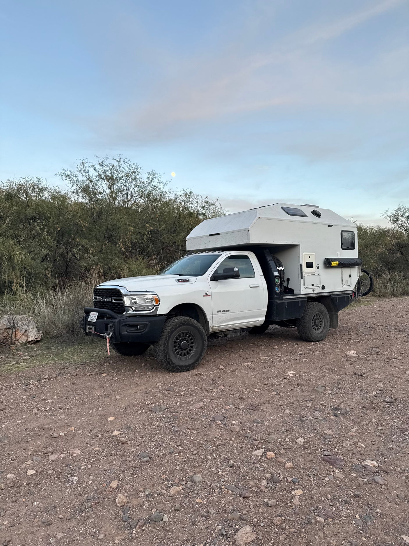 White Ram 3500 truck with off-road overland camper, perfect for an RV rental adventure on gravel. Moon in sky.