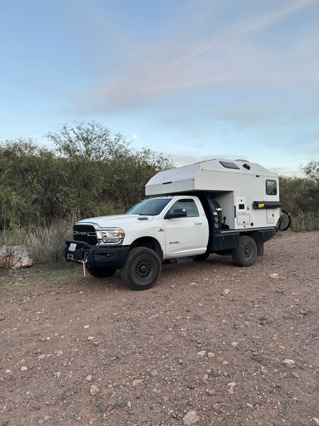 White Ram 3500 truck with off-road overland camper, perfect for an RV rental adventure on gravel. Moon in sky.