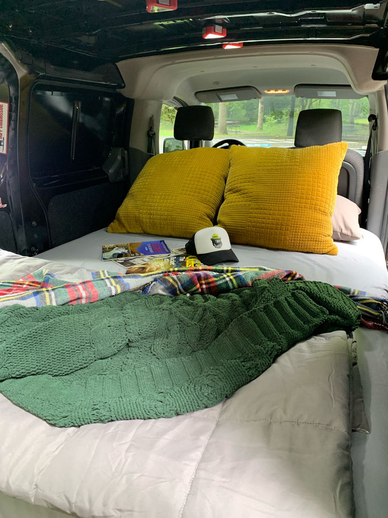 Cozy RV rental bed with yellow pillows, plaid & green blankets, magazines, and a hat, ready for travel. — photo 2