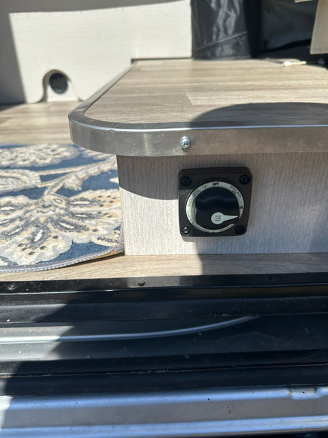 Power management on an rv rental: a Blue Sea battery switch set to 'OFF,' mounted on a wood-grain panel.