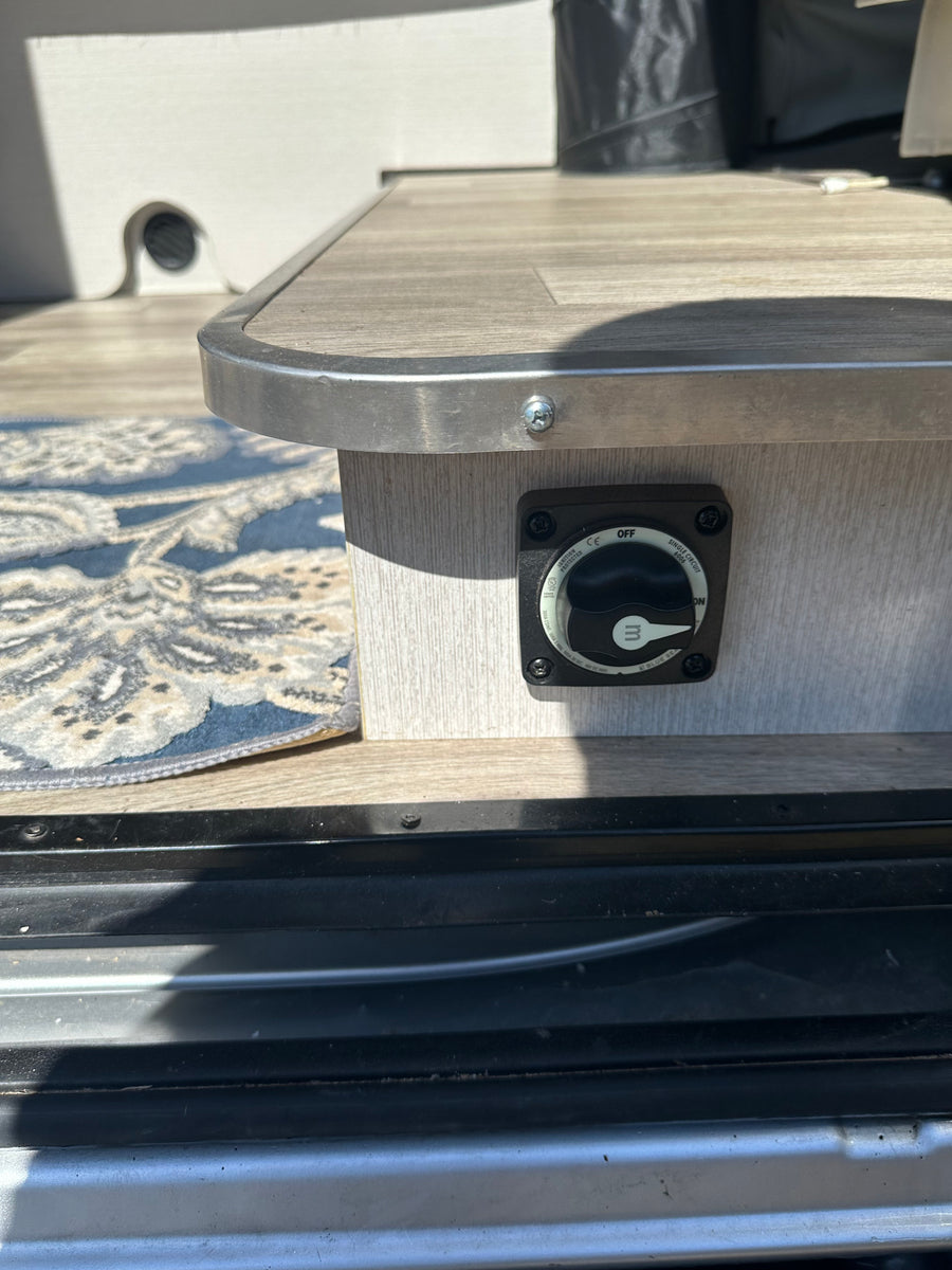 Power management on an rv rental: a Blue Sea battery switch set to 'OFF,' mounted on a wood-grain panel.