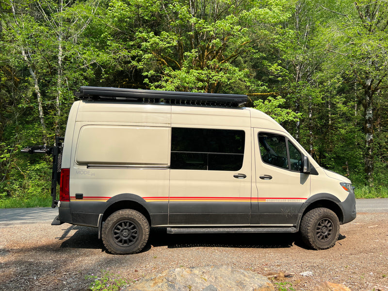 A cream-colored Storyteller Overland 4x4 camper van, ideal for RV rental adventures, parked by a lush forest. — photo 7