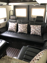 Relax in style with this RV rental's black leather sofa, featuring patterned pillows and bright windows for a comfortable journey.