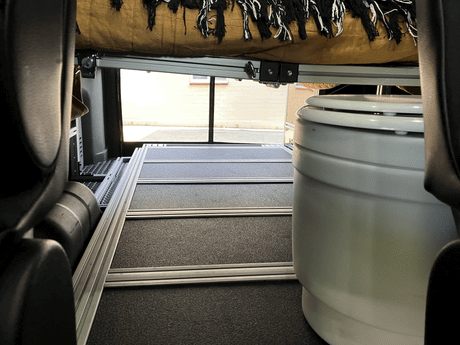Interior of an RV rental: raised bed above a modular floor system and a portable toilet.