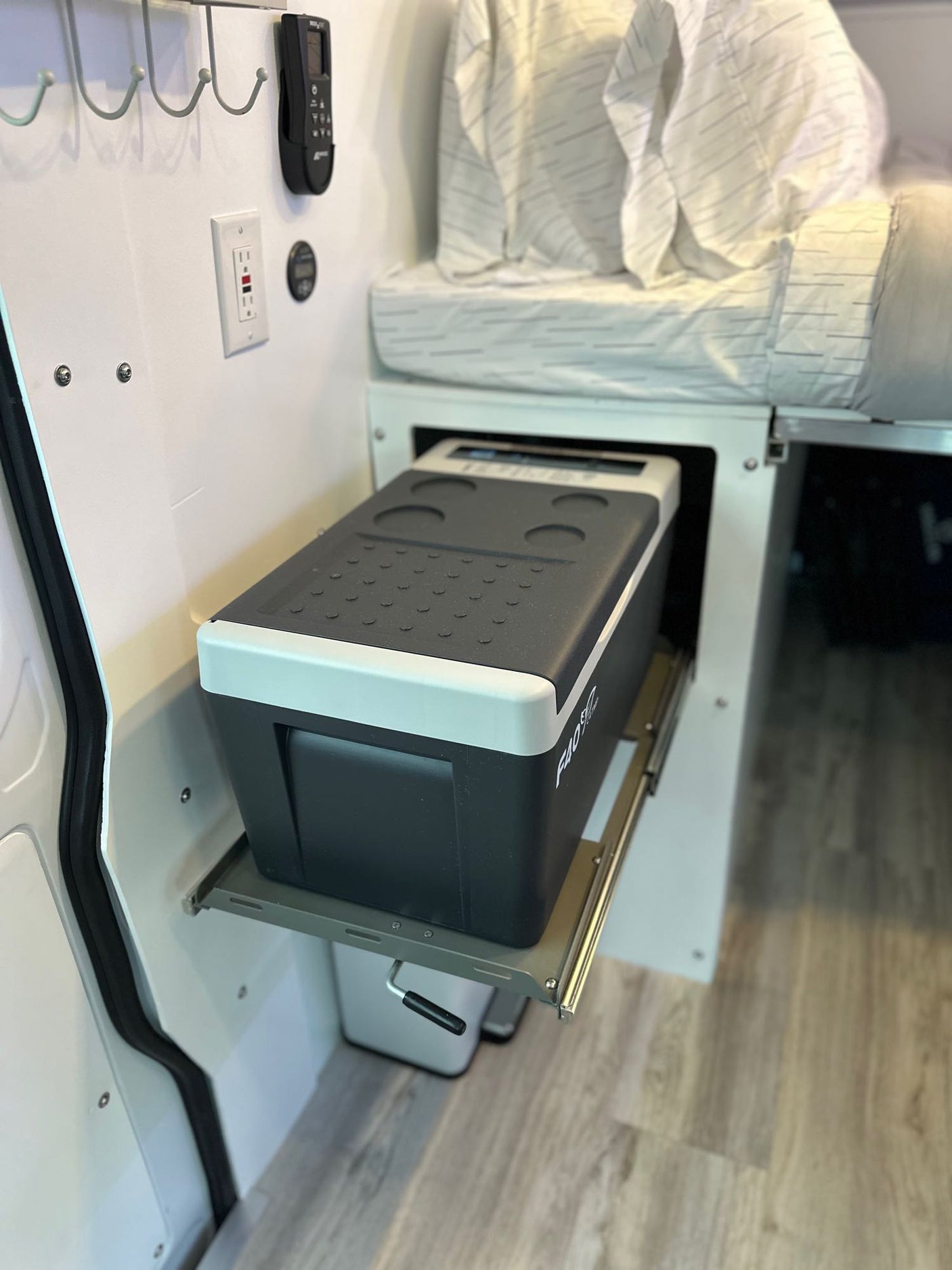 Inside an rv rental: Portable fridge on a slide-out, bed, and outlet for comfortable camper van living.