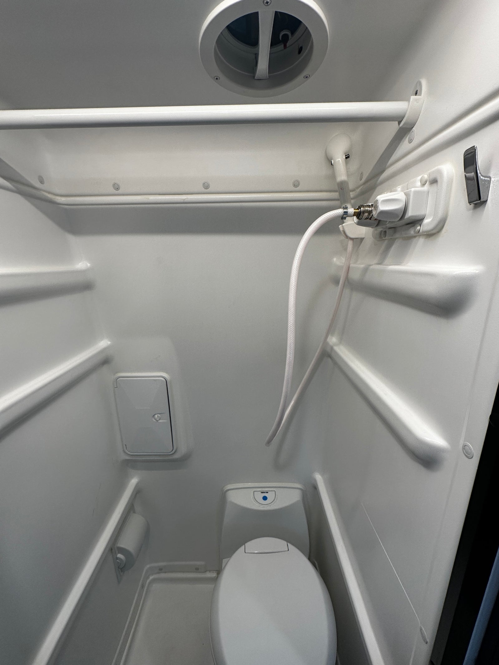 This RV rental wet bath features a toilet, handheld shower, overhead vent, and storage, all in a compact space.