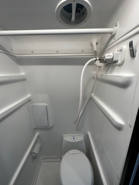 This RV rental wet bath features a toilet, handheld shower, overhead vent, and storage, all in a compact space.