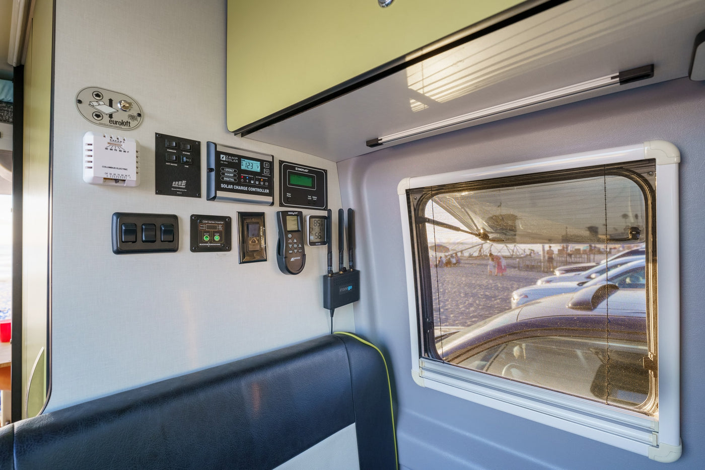 RV rental interior: Control panel displays for solar, inverter, HVAC, and Euroloft bed. Mobile internet and beach window view. — photo 16