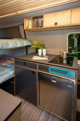 Modern RV rental interior: compact kitchen with stove, fridge, and cozy bunk beds, all in a smartly designed space.
