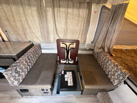 Pop-up RV rental interior: Dinette seating, a stowed table, portable stove, and tent walls with exit sign.