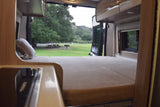 Cozy RV rental interior with bed & kitchen, opening to a peaceful campsite with a picnic table and trees.