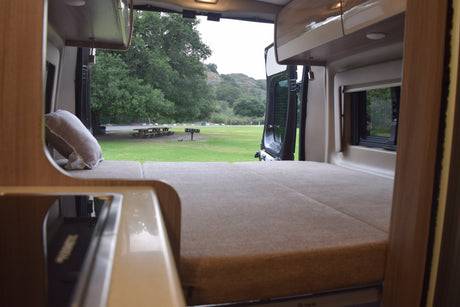 Cozy RV rental interior with bed & kitchen, opening to a peaceful campsite with a picnic table and trees.