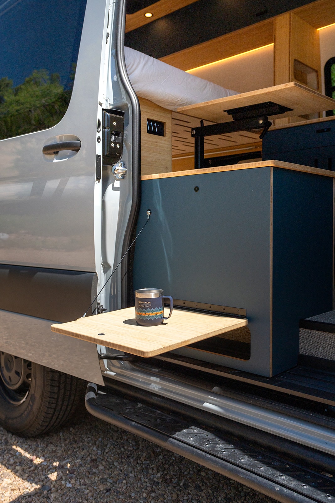 Custom camper van interior for RV rental adventures. Features a cozy bed, pull-out table & clever storage. — photo 6