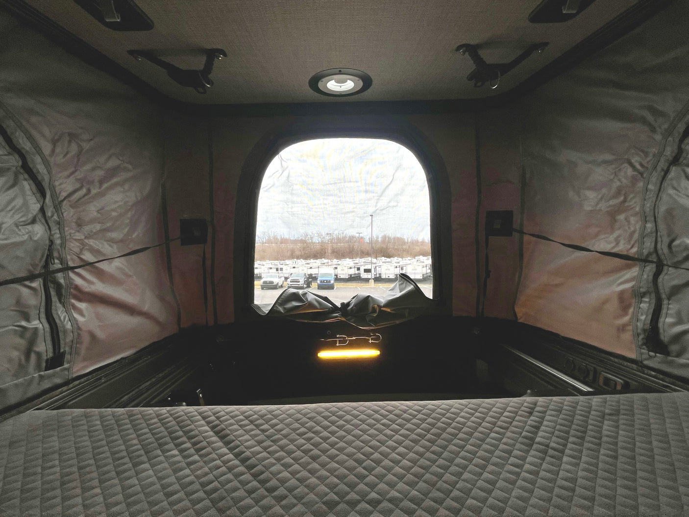 Cozy pop-top interior with a quilted bed, overlooking an RV rental lot. Perfect for travel and camping adventures.