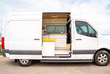 This custom white camper van, perfect for an RV rental, shows its open side door revealing a stylish kitchen and cozy interior setup for travel.