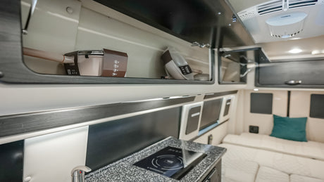 Modern RV rental interior with a compact kitchen, overhead storage, and lounge area.