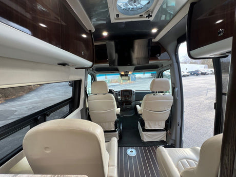 View inside a luxurious RV rental, featuring cream leather seats, polished wood cabinets, and an overhead TV.
