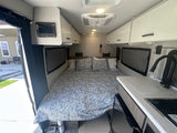 This RV rental interior showcases a comfy bed, compact kitchen with sink/stove, and overhead cabinets.