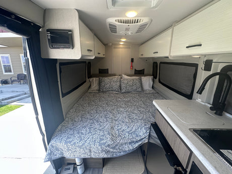 This RV rental interior showcases a comfy bed, compact kitchen with sink/stove, and overhead cabinets.