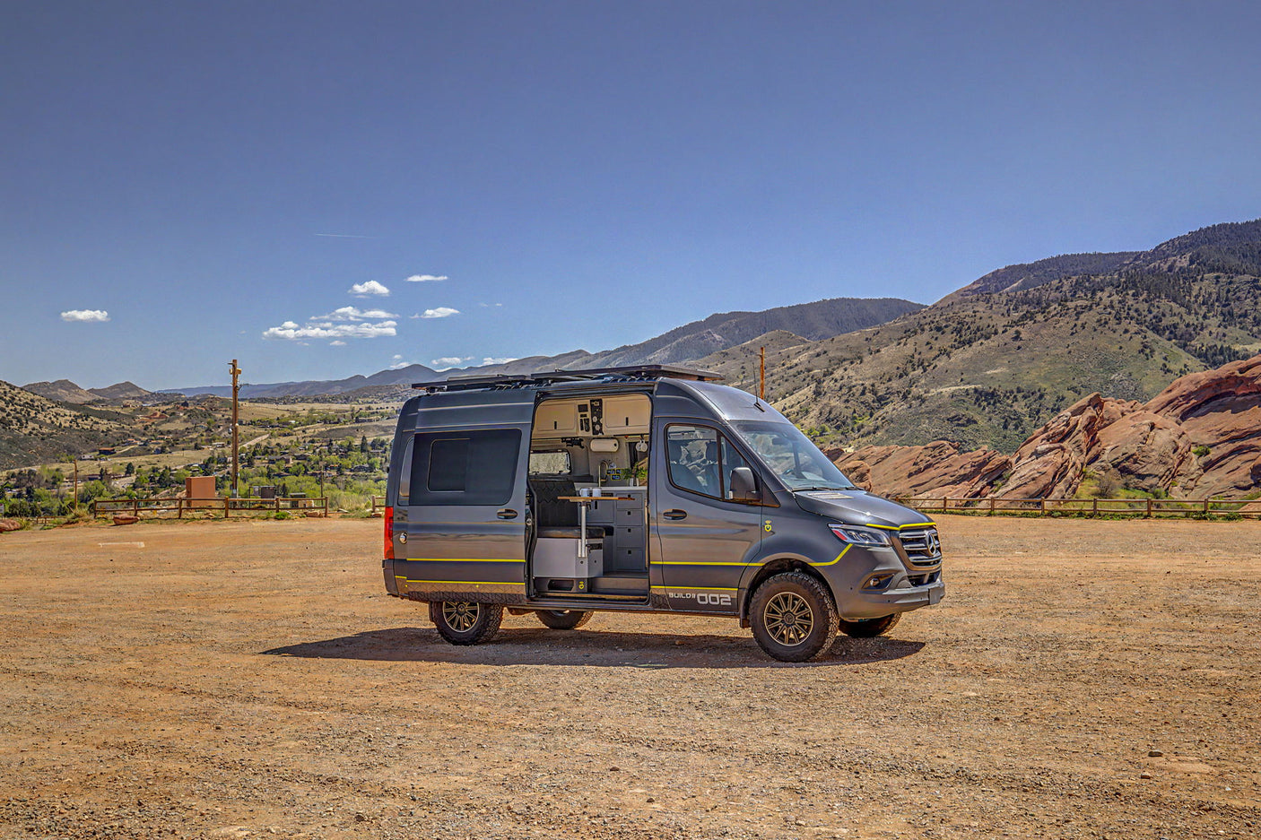 Custom grey Sprinter camper van, door open revealing interior, parked on dirt in mountains. Ideal for rv rental adventures.