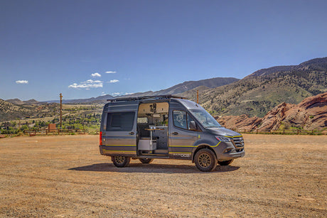 Custom grey Sprinter camper van, door open revealing interior, parked on dirt in mountains. Ideal for rv rental adventures.