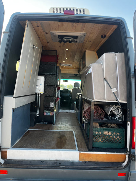 Inside an RV rental van, featuring a custom shower, wooden ceiling, bed, and storage. Ready for adventure.