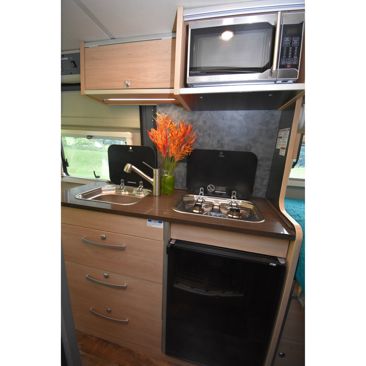 Efficient Hymer RV rental kitchen: sink, two-burner stove, microwave, and wooden storage for convenience.
