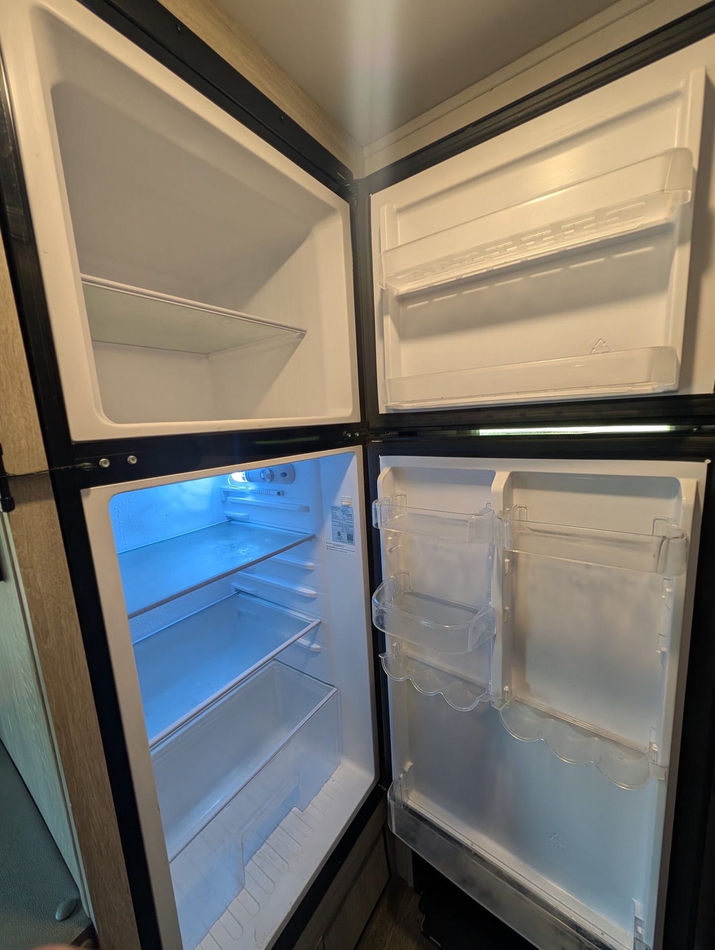 Clean, empty two-door RV refrigerator, open for your rv rental. Blue light illuminates shelves with condensation. — photo 7