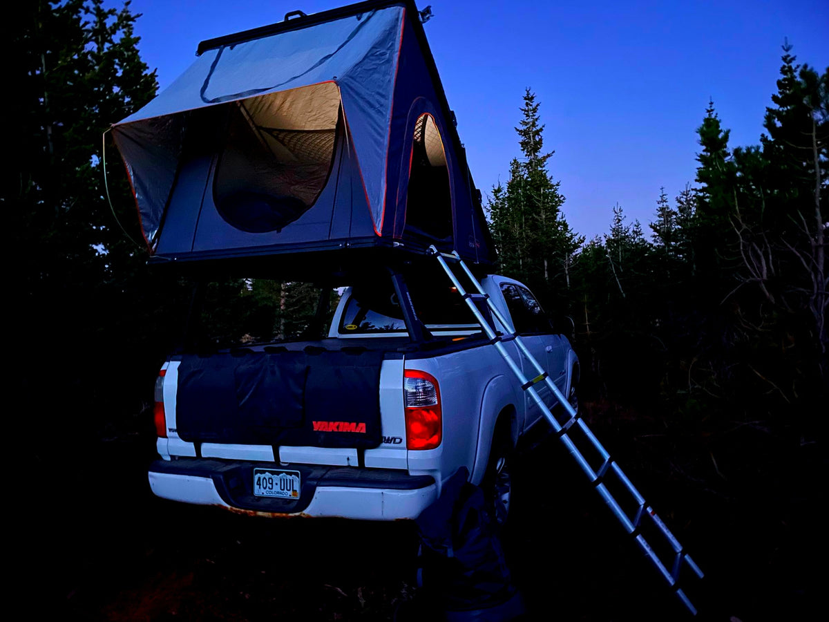 A white pickup truck with a lit rooftop tent and ladder, an excellent RV rental option for overlanding adventures at dusk. — photo 7