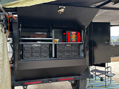 This RV rental's rear compartment is open, revealing neatly organized shelves with collapsible crates, bags, and camping gear.
