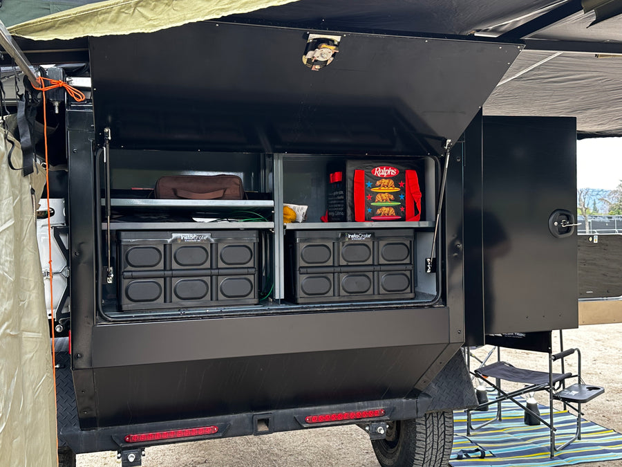 This RV rental's rear compartment is open, revealing neatly organized shelves with collapsible crates, bags, and camping gear.