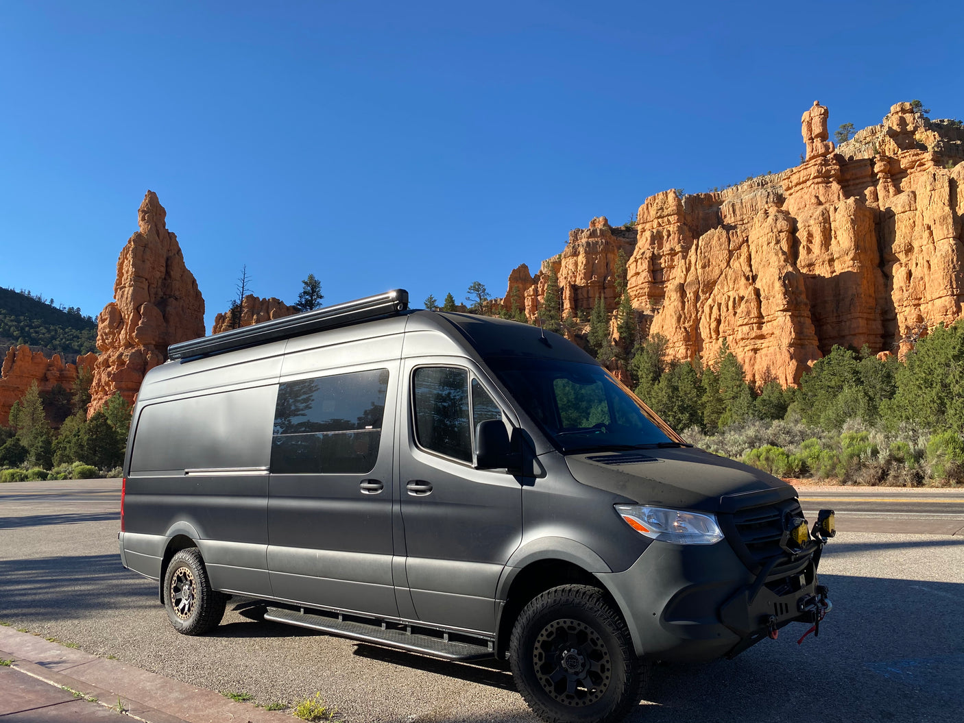A sleek grey RV rental, equipped for adventure, parked in a stunning red rock landscape under a clear blue sky.